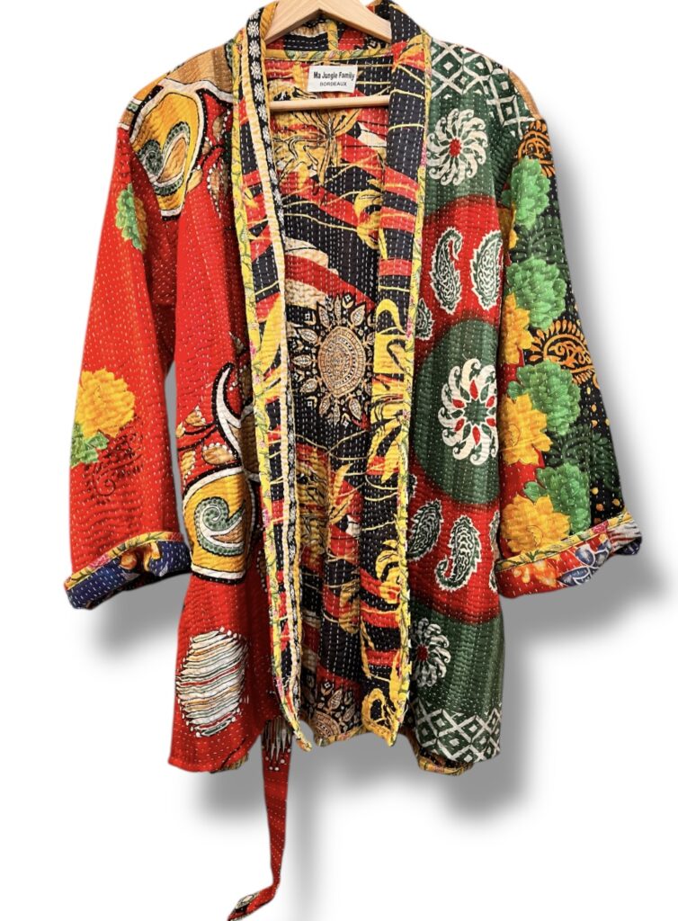 Veste kantha vintage réversible en coton recyclé, faite main à partir de saris indiens – pièce unique aux motifs fleuris colorés, exposée sur un portant. Rouge, vert, fleurs