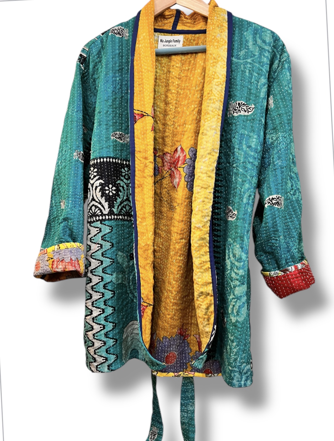 Veste kantha vintage réversible en coton recyclé, faite main à partir de saris indiens – pièce unique aux motifs fleuris colorés, exposée sur un portant. Rouge, vert, fleurs, orange, reversilble, turquoise, jaune, upcycling
