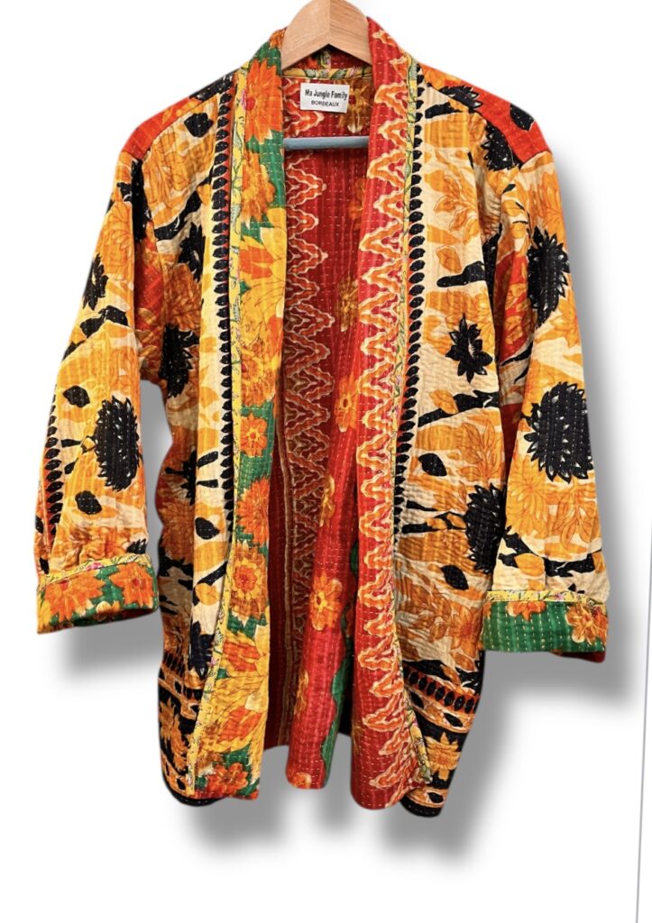 Veste kantha vintage réversible en coton recyclé, faite main à partir de saris indiens – pièce unique aux motifs fleuris colorés, exposée sur un portant. Rouge, vert, fleurs, orange, reversilble